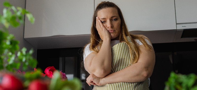 A woman sits in front of a bathroom scale, head down, overwhelmed with emotion—symbolizing the emotional toll behind weight loss struggles.
